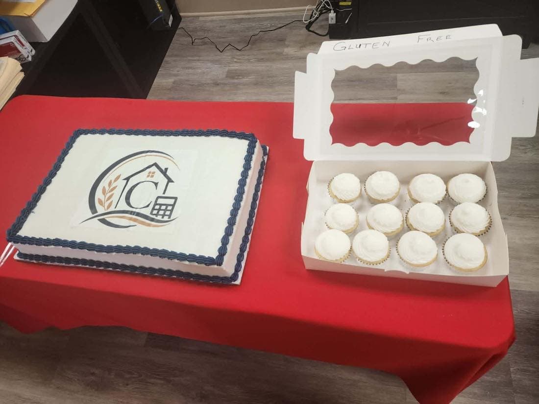 A grand opening sheet cake decorated with the Capps Family Tax logo, beside a box of gluten free cupcakes.