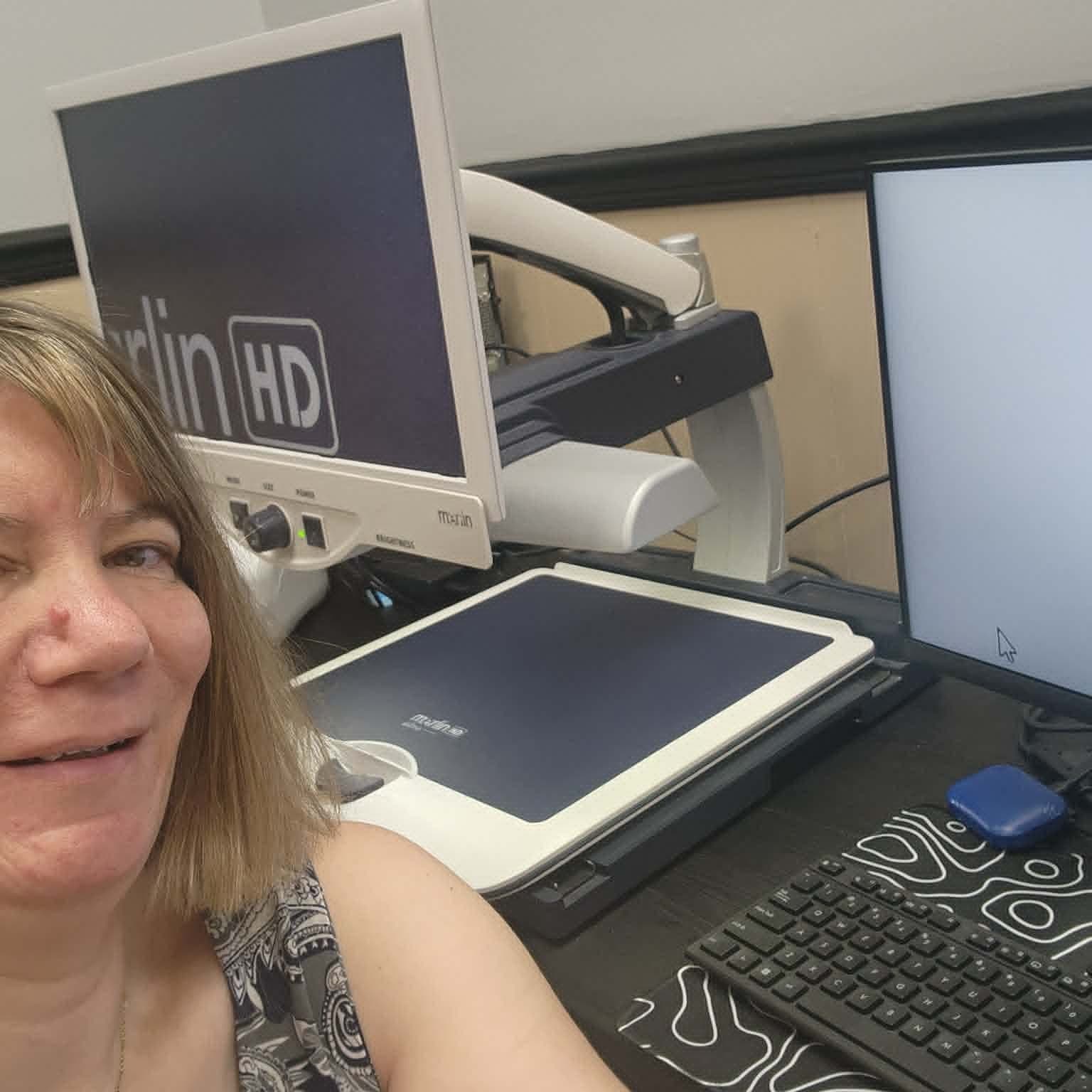 Sherri Capps at her desk in the Lyons office, working with her video magnifier.